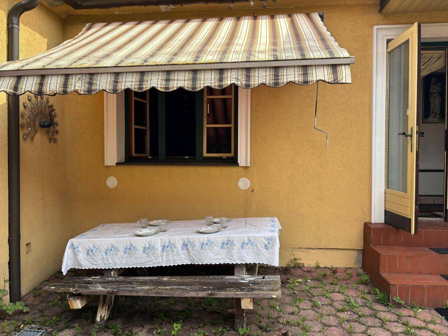 Einfacher Außenbereich mit Markise, Holztisch und Bank, ideal für Mahlzeiten im Freien.