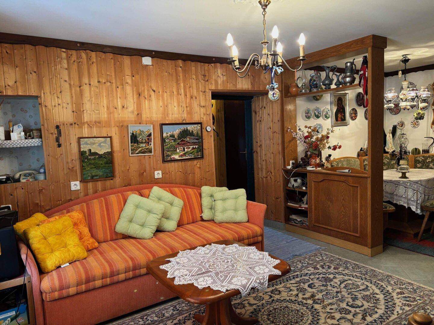 Gemütliches Wohnzimmer mit Holzvertäfelung, gestreiftem Sofa und traditionellem Teppich.