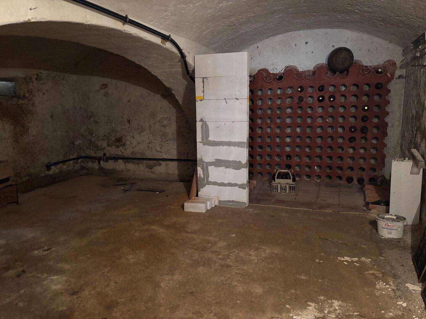 Geräumiger Kellerraum mit Gewölbedecke und einer Wand für Weinflaschenlagerung.