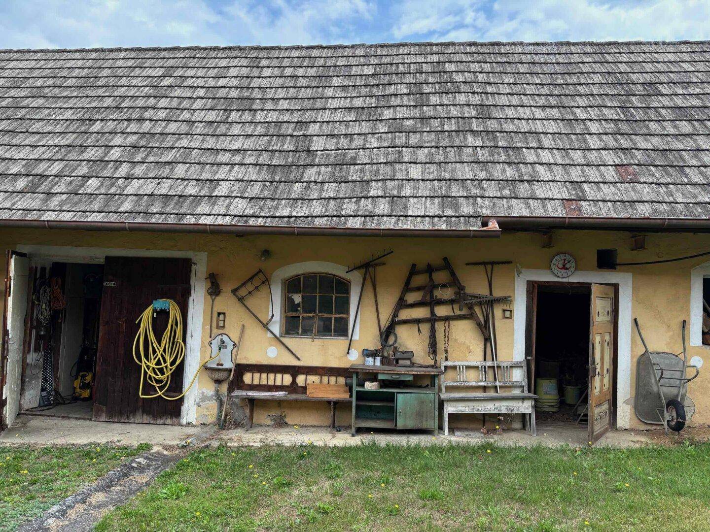 Traditionelle Hausfassade mit Holzdach, Werkzeugen und Geräten an der Wand.