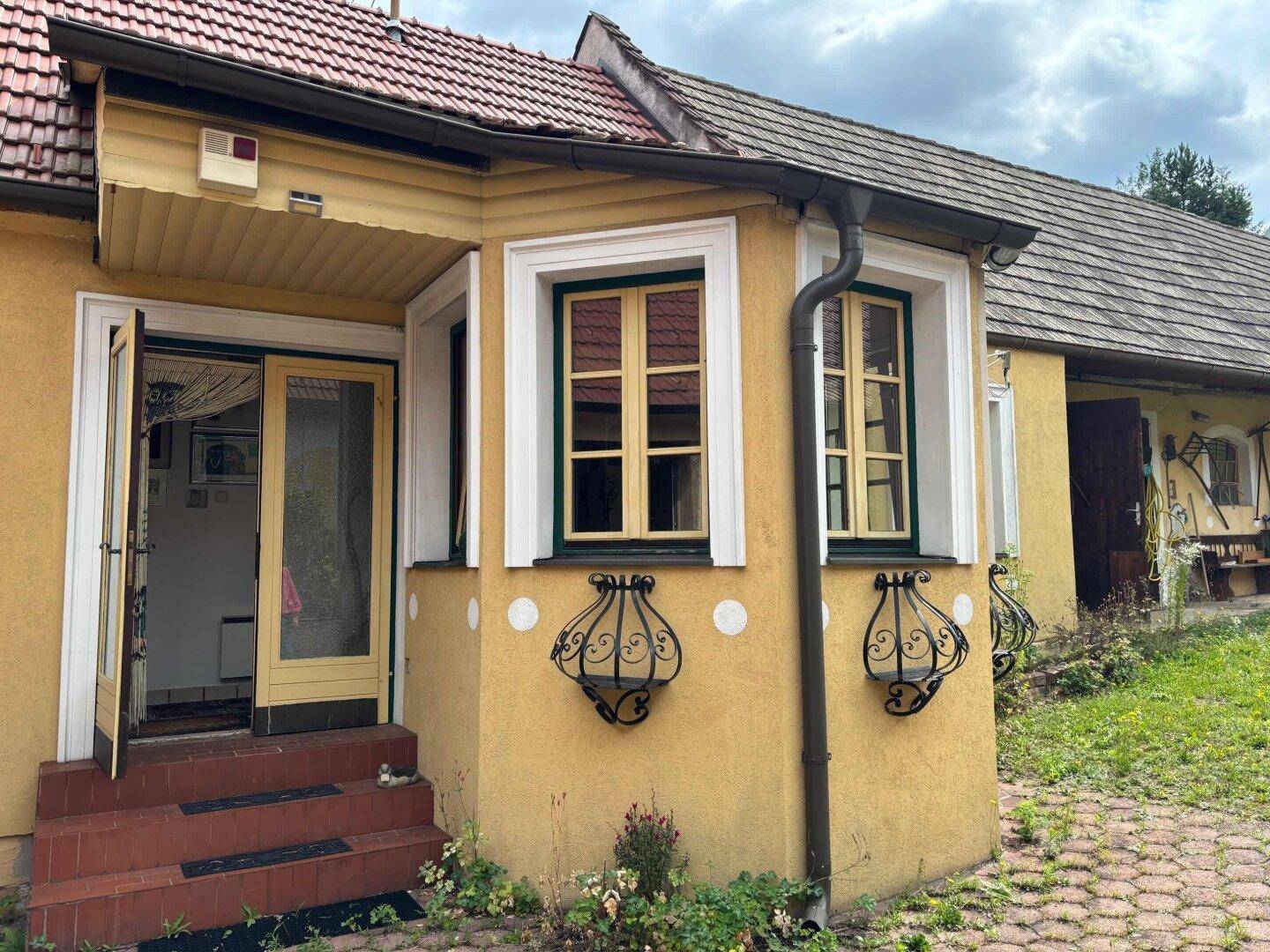 Eingangsbereich eines traditionellen Hauses mit gelber Fassade und verzierten Fenstergittern.