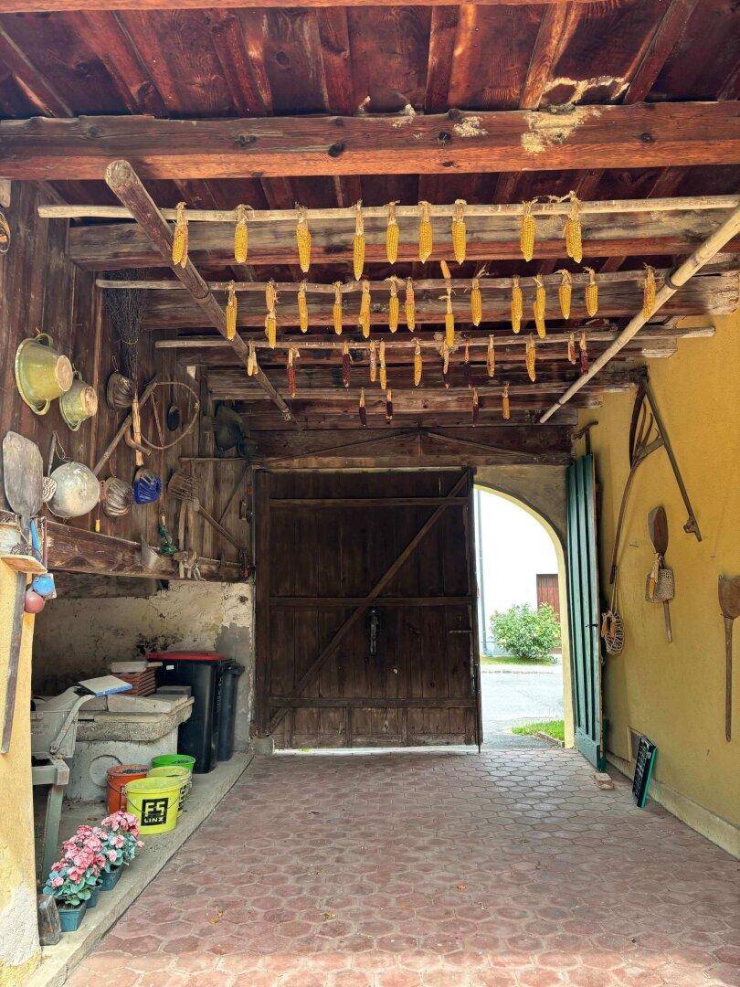 Rustikaler Durchgangsbereich mit Holzbalken, gepflastertem Boden und getrocknetem Mais an der Decke.