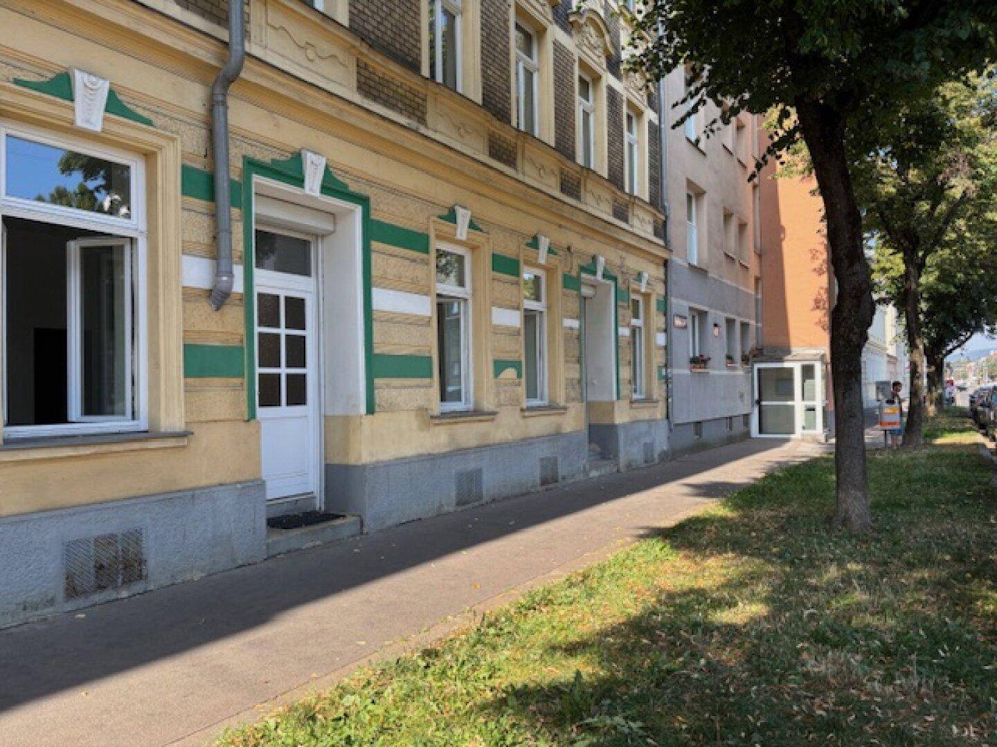Seitenansicht der historischen Fassade mit Bäumen und Bürgersteig an einem sonnigen Tag.