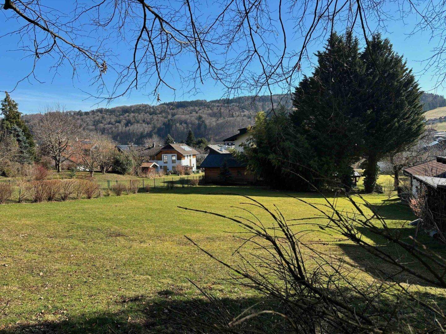 Ausgedehnte grüne Wiese mit Blick auf bewaldete Hügel und weitere Häuser in der Ferne.