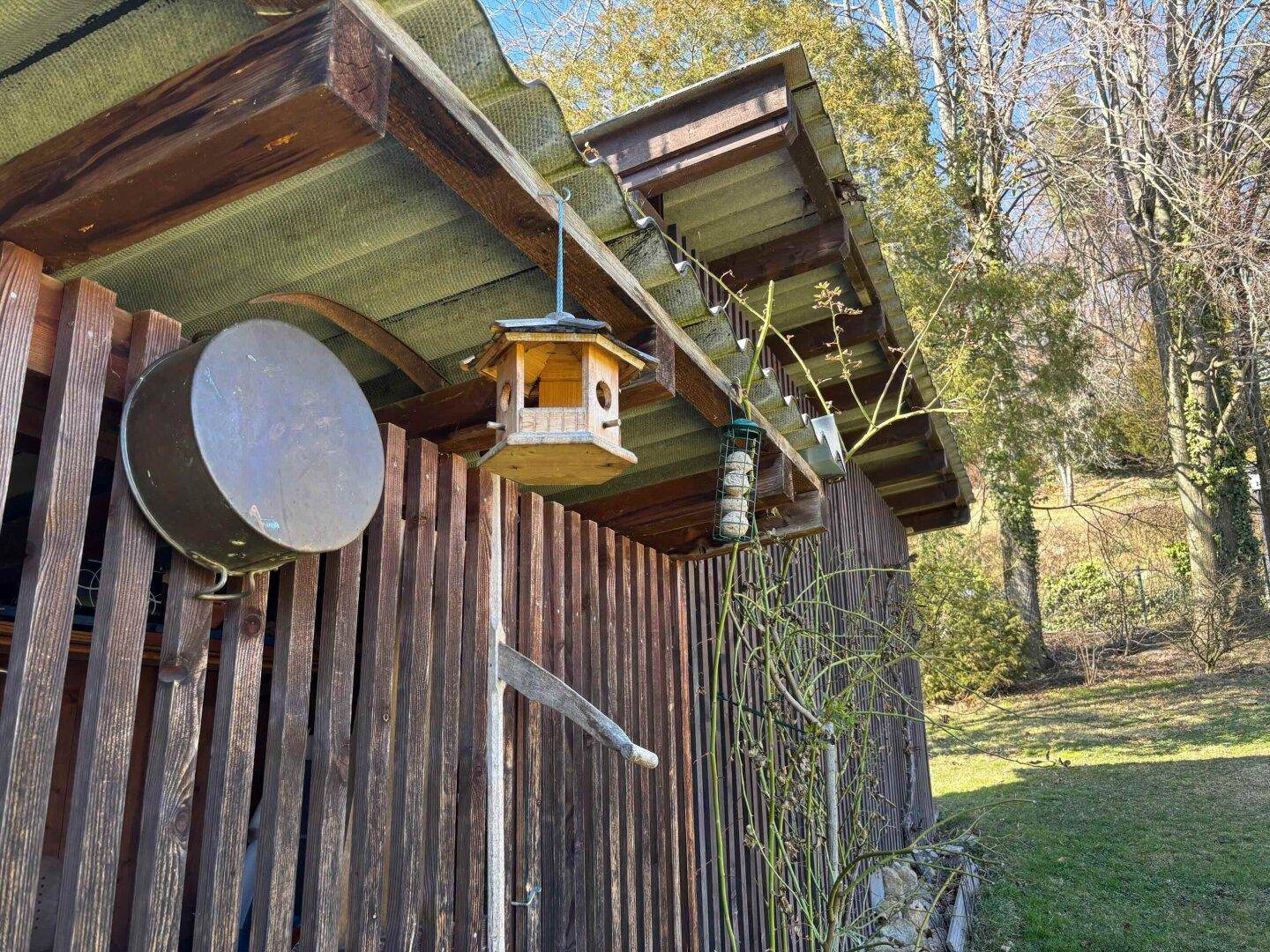 Nahaufnahme eines rustikalen Holzschuppens mit Vogelhäuschen und Futterstellen im Gartenbereich.
