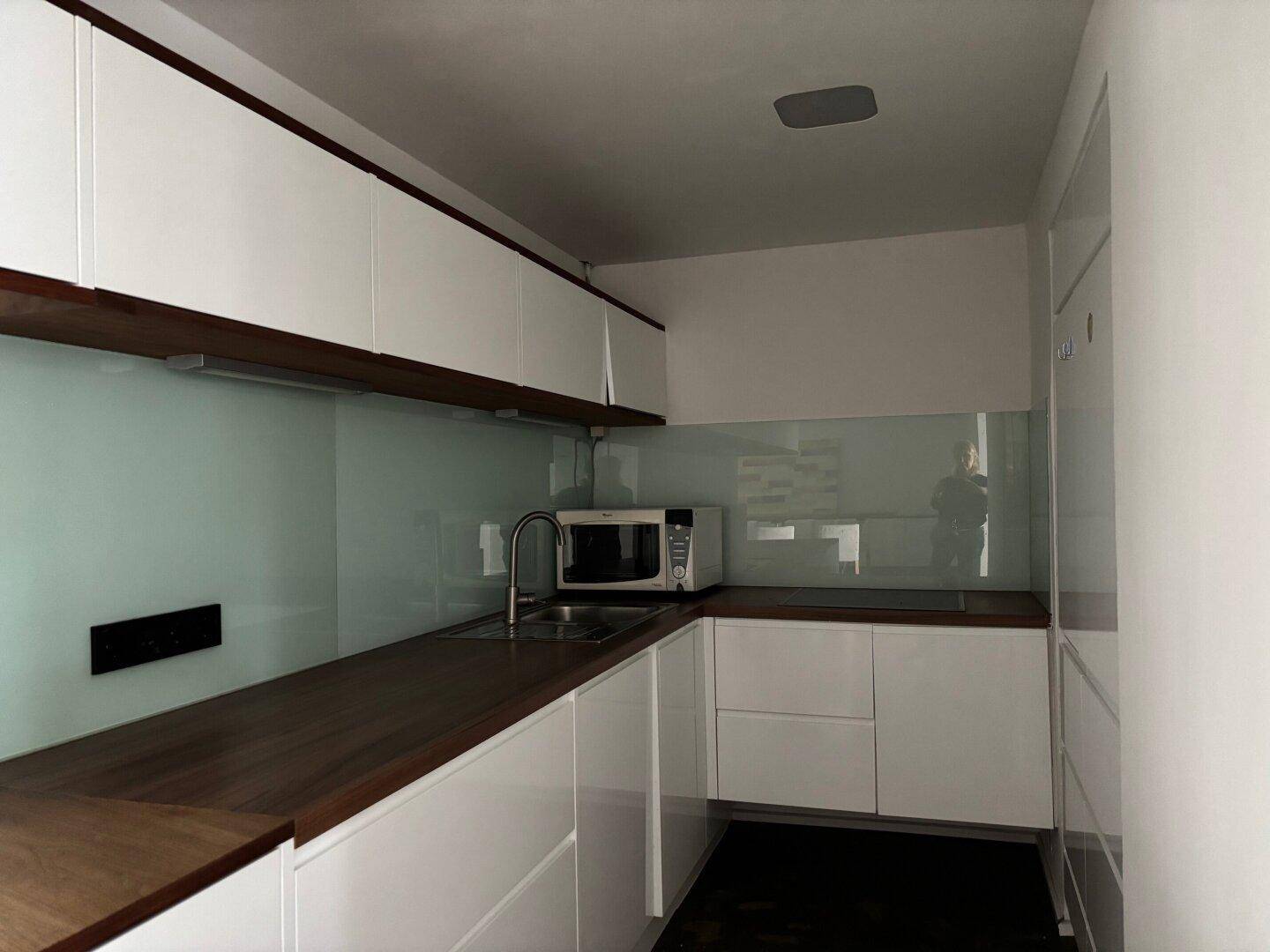 Moderne Küche mit weißen Hochglanzschränken, dunklen Holz-Arbeitsplatten und integrierter Mikrowelle.