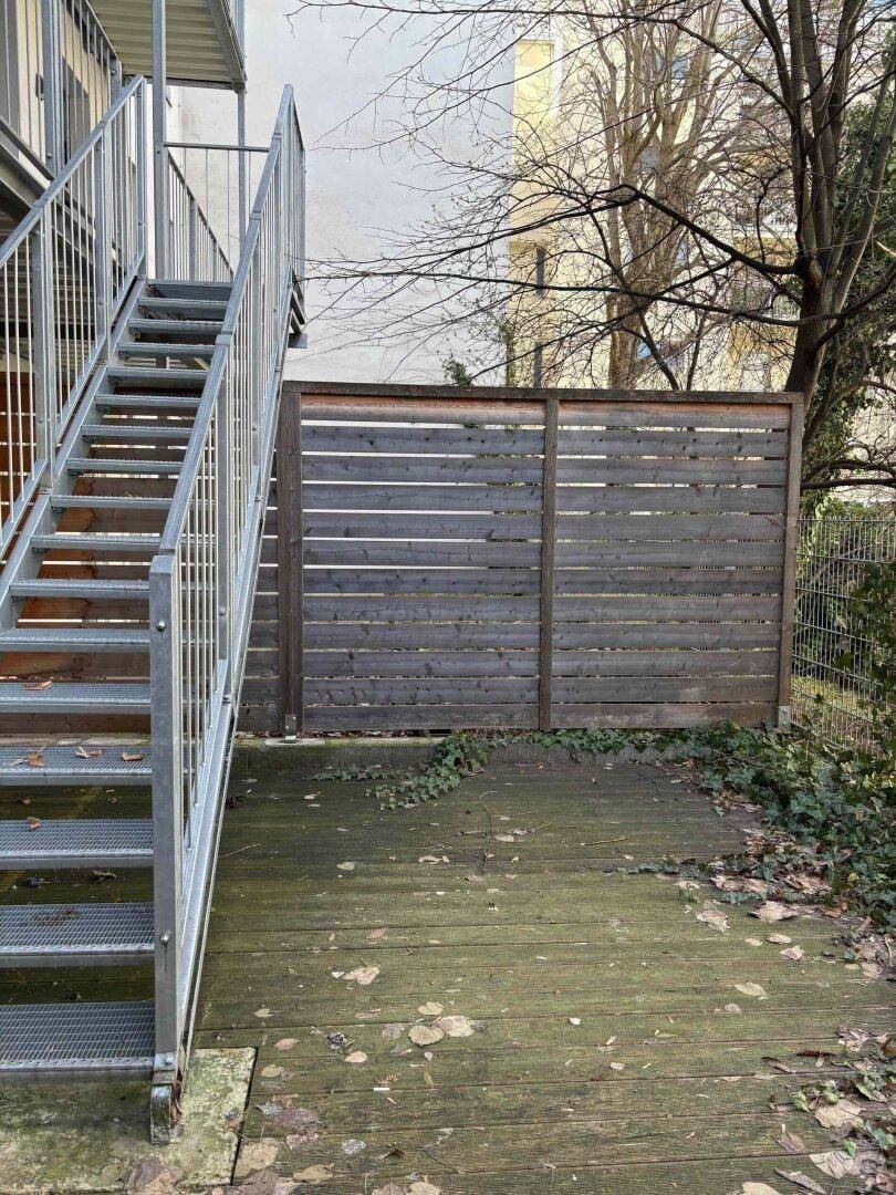 Hinterhofbereich mit Holzterrasse, Metalltreppe und einem Holzzaun, der Privatsphäre bietet.