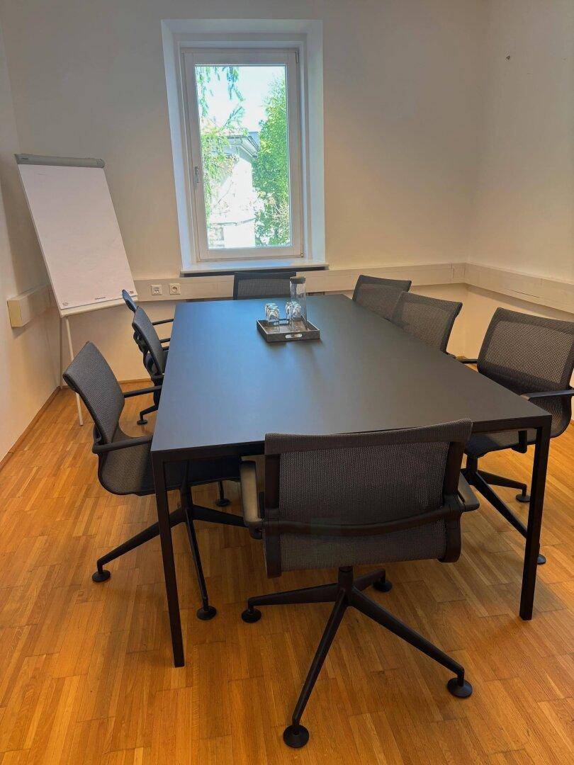 Moderner Konferenzraum mit dunklem Tisch, bequemen Stühlen und einem Flipchart für Präsentationen.