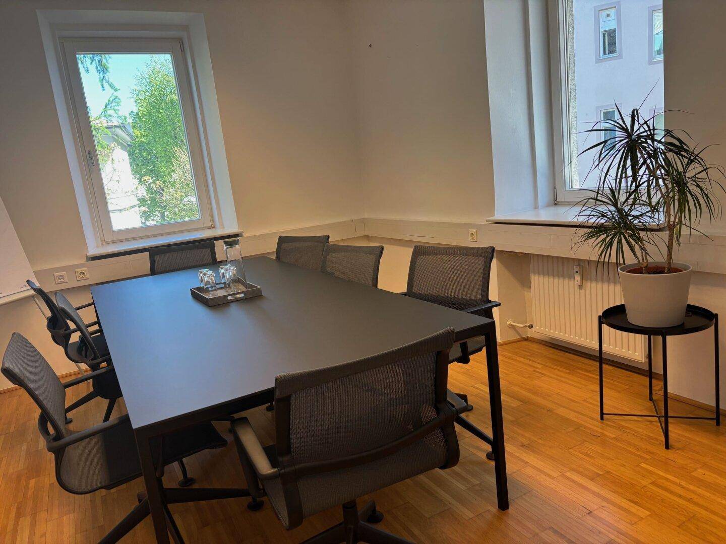 Konferenzraum mit großem dunklen Tisch, ergonomischen Stühlen und einem Fenster mit Blick ins Grüne.