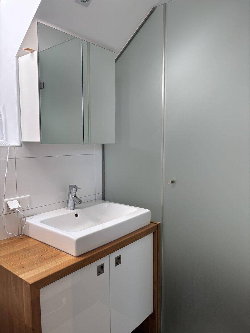 Modernes Badezimmer mit Waschbecken, Spiegelschrank und Duschkabine aus Milchglas.