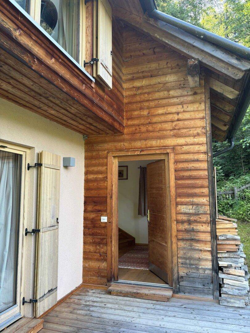 Eingangsbereich des Holzhauses mit Holztür, Fensterläden und einer Holzterrasse.