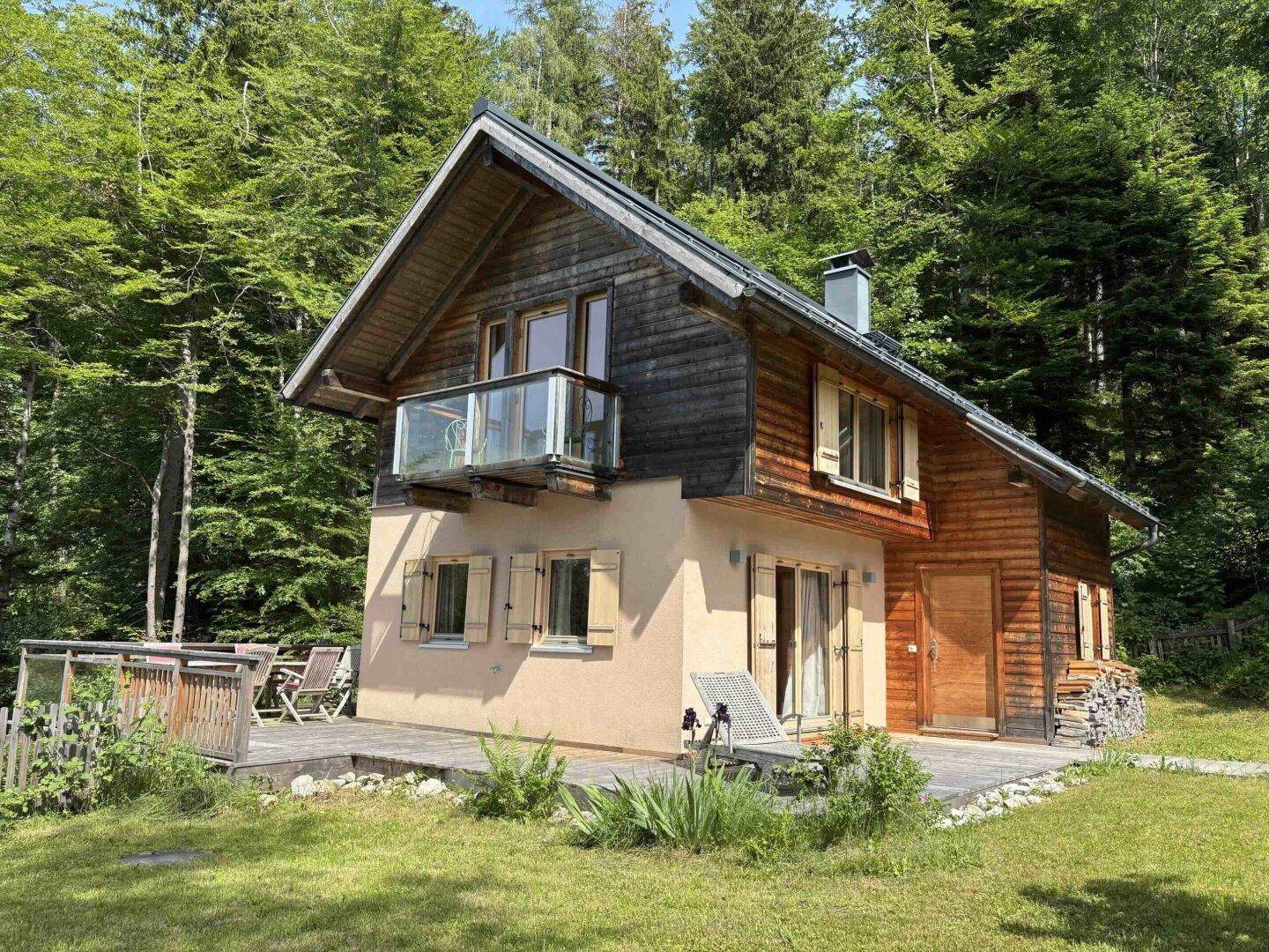 Charmantes Holzhaus mit Balkon, Terrasse und Garten, eingebettet in grüne Landschaft.