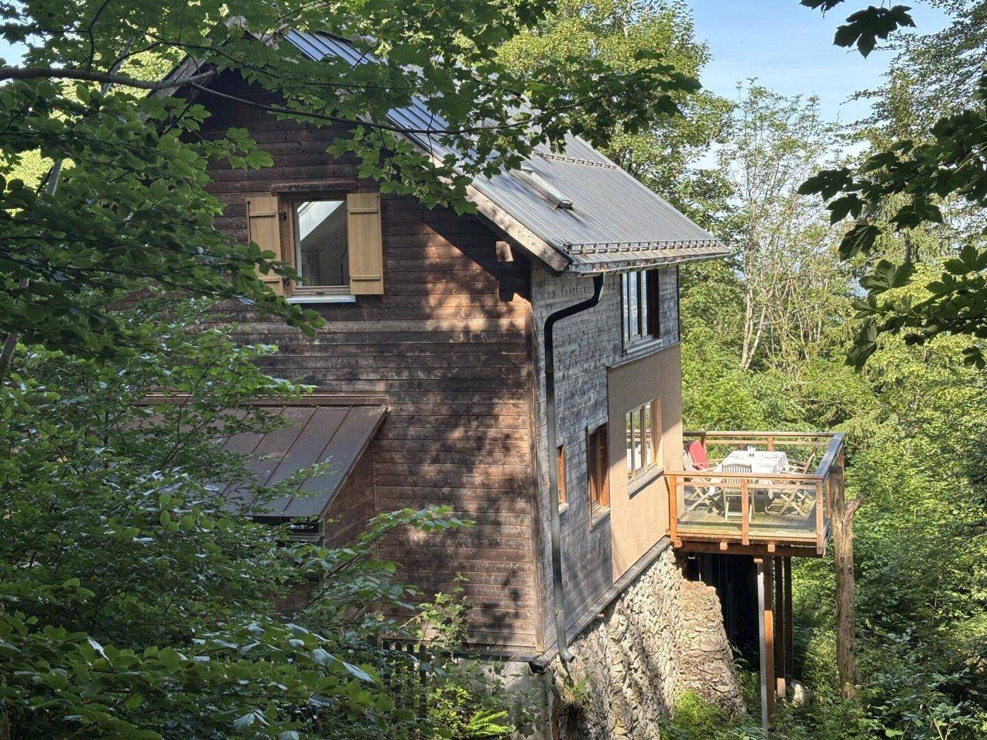 Charmantes Holzhaus in Hanglage mit seitlicher Terrasse und umgebendem Wald.