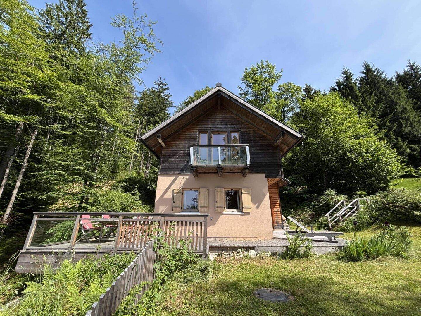 Freistehendes Holzhaus mit Balkon und Terrasse, umgeben von üppiger Natur.