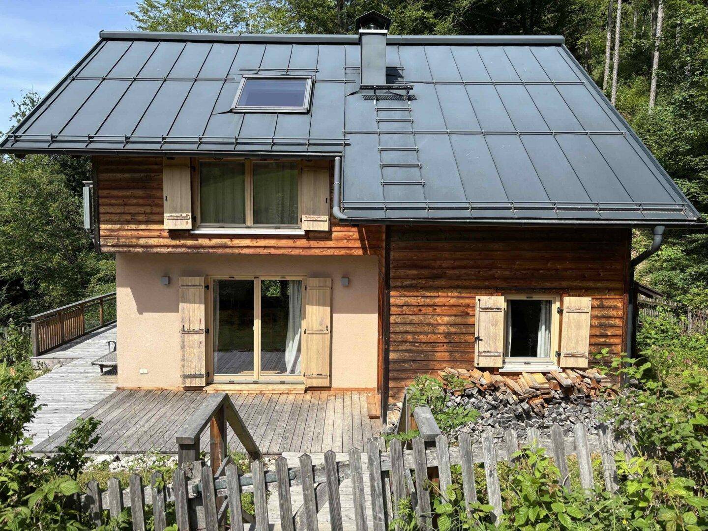 Charmantes Holzhaus mit modernem Metalldach, großer Holzterrasse und umgebender Natur.