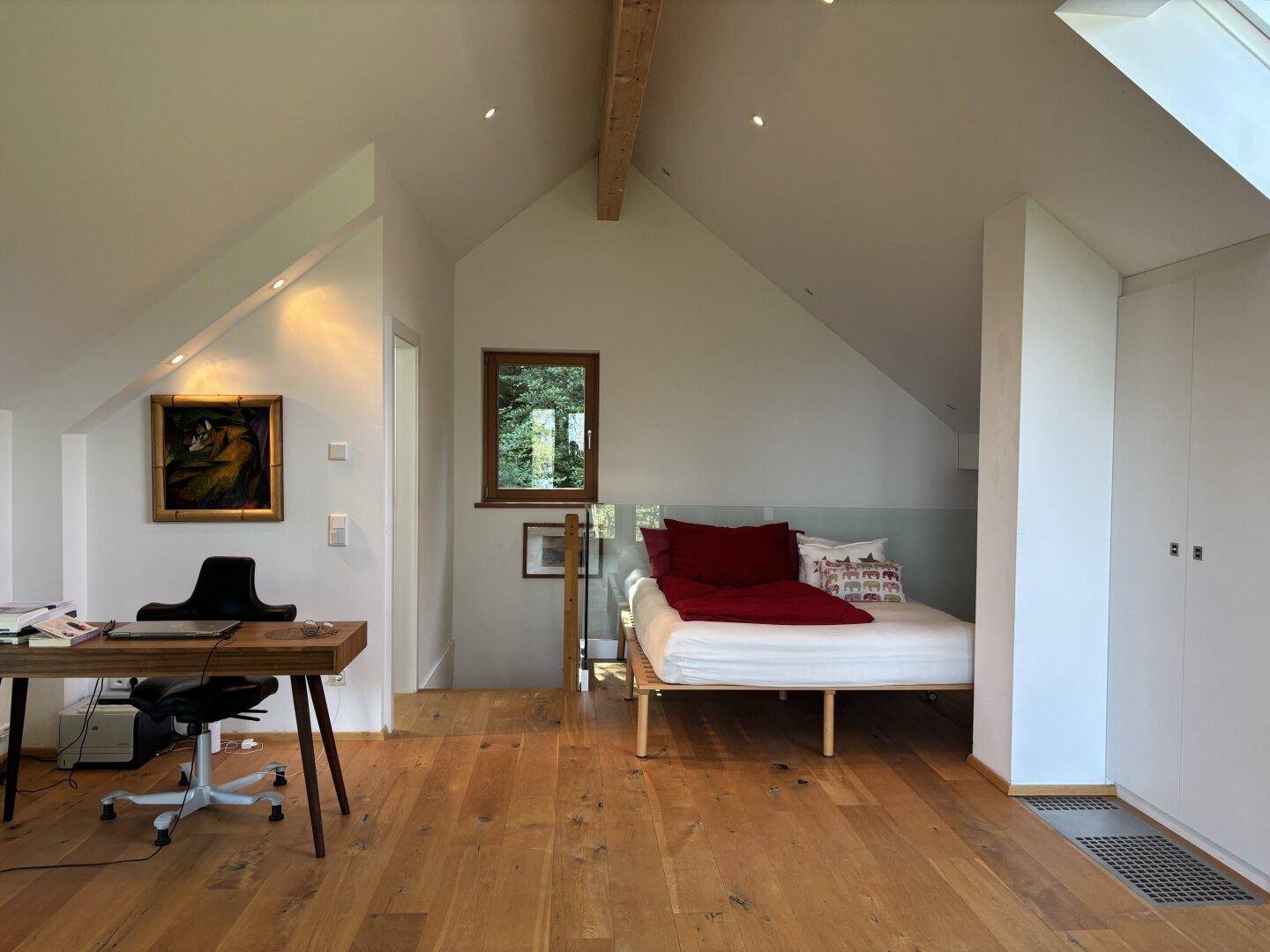 Schlafzimmer im Dachgeschoss mit Holzboden, Schreibtisch und integrierten Schränken.