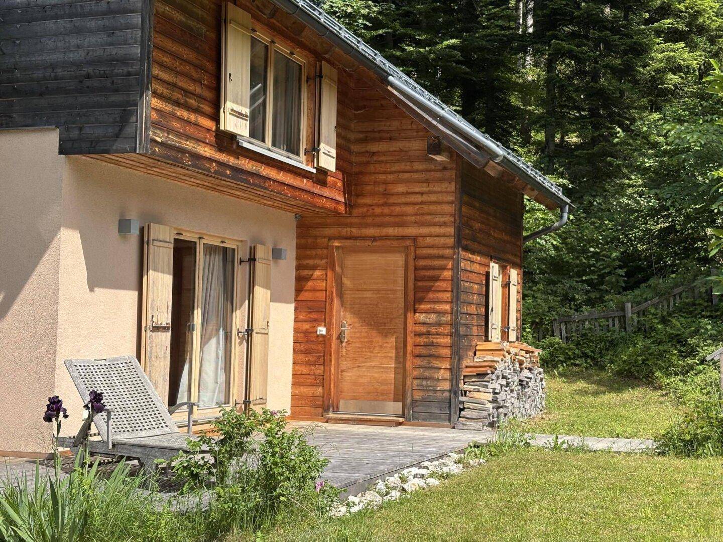 Holzhaus mit Terrasse und Rasenfläche, umgeben von Bäumen und Natur.