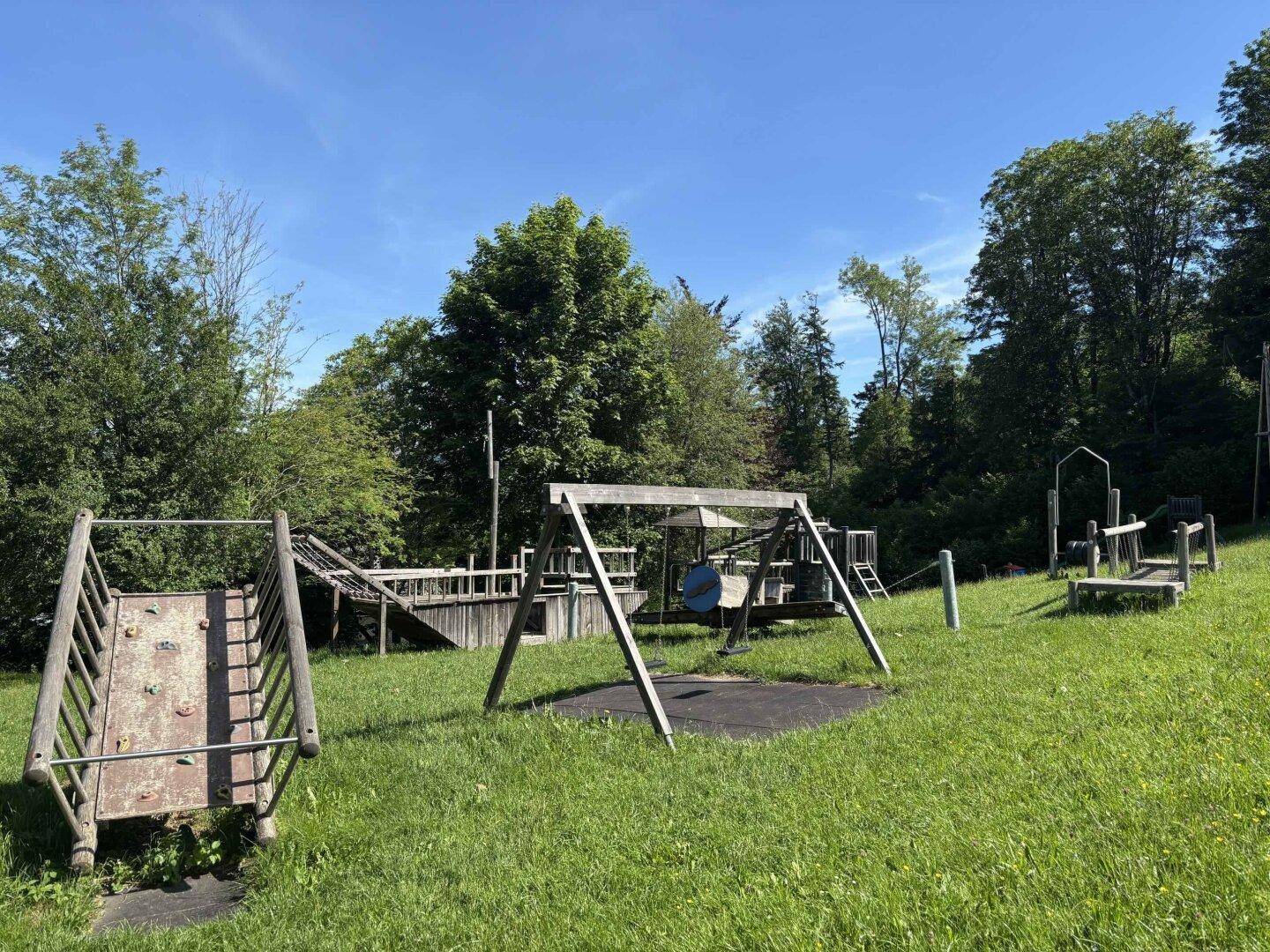 Großer Kinderspielplatz mit Schaukeln, Rutschen und Klettergeräten in grüner Umgebung.