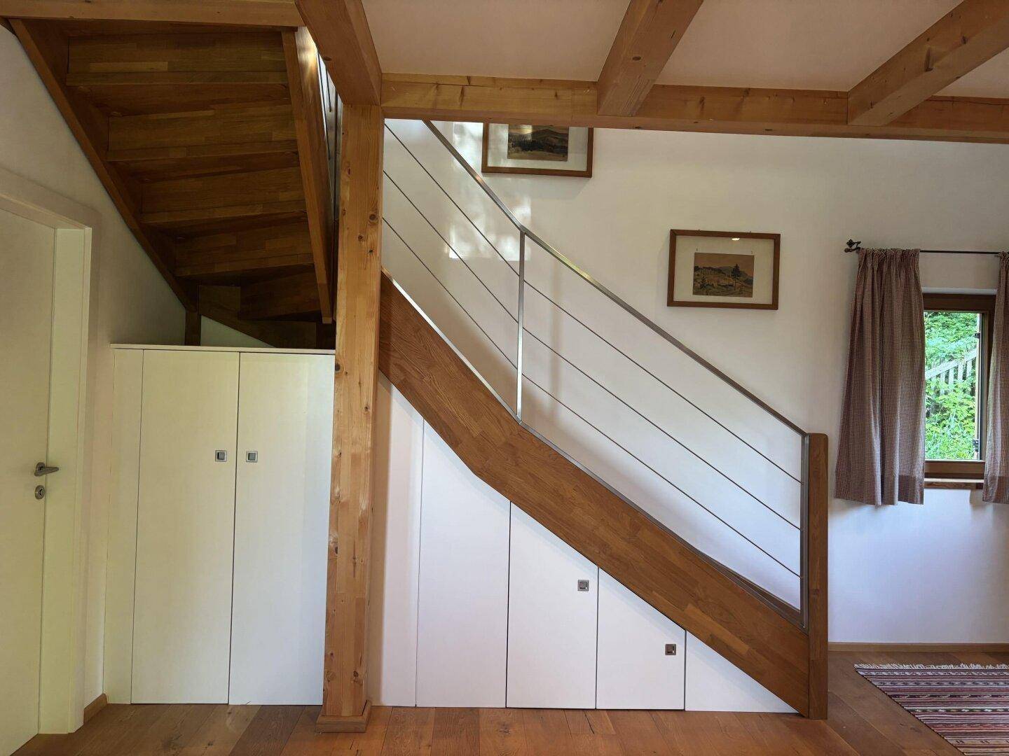 Heller Flur mit Holztreppe, integrierten Schränken und Holzbalken an der Decke.