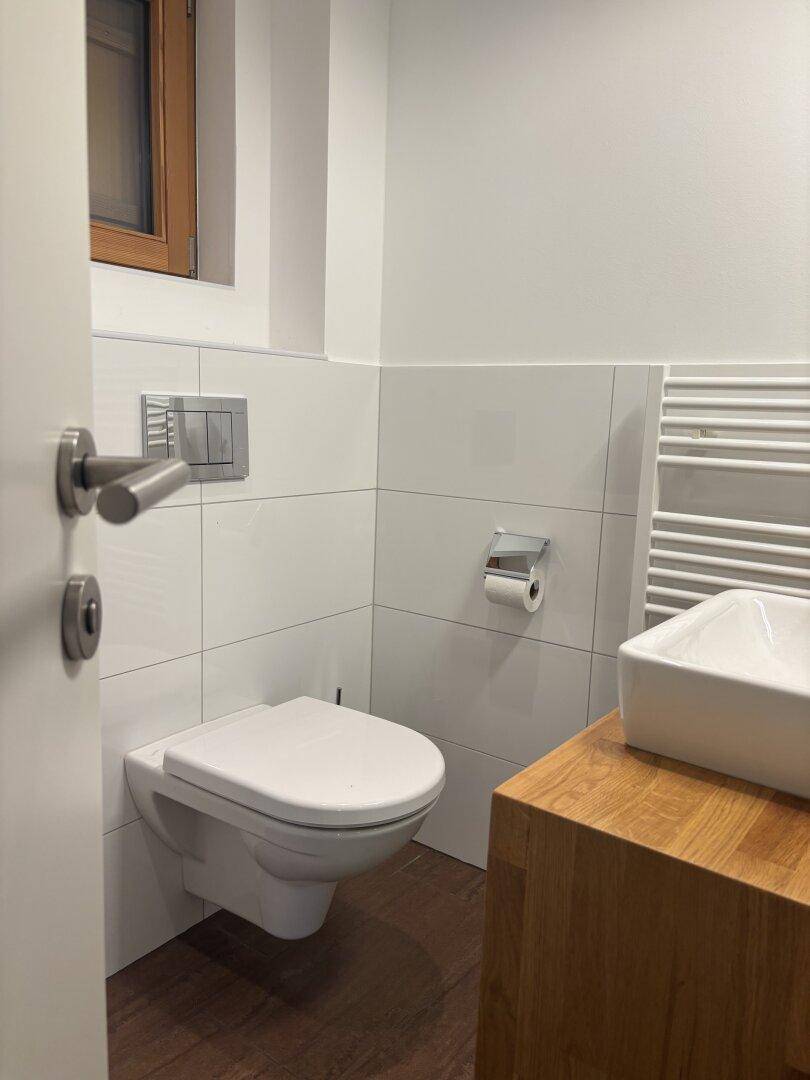 Modernes Gäste-WC mit wandhängendem WC, Waschbecken und beheiztem Handtuchhalter.