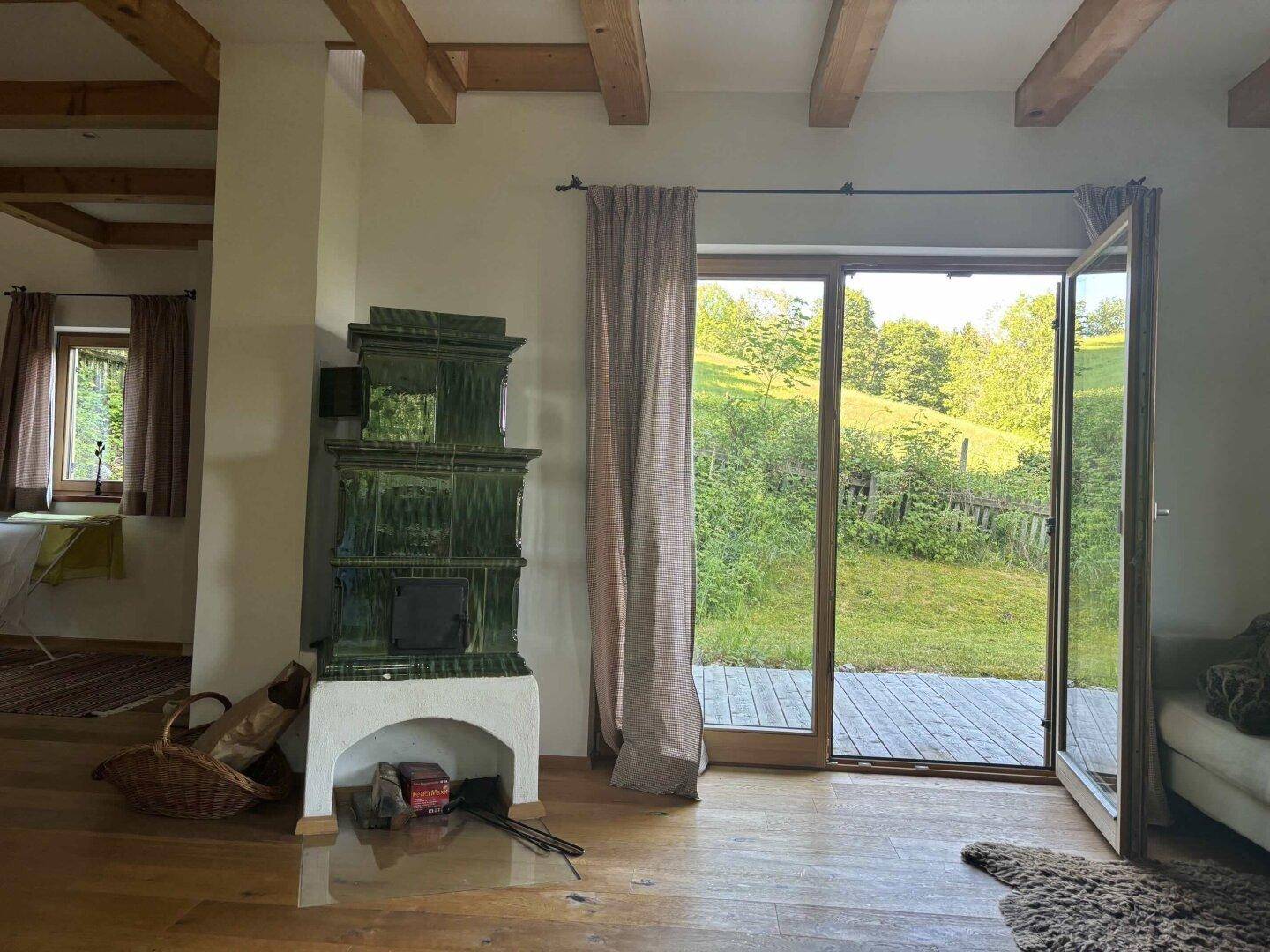Gemütliches Wohnzimmer mit traditionellem Kachelofen, Holzbalken und Zugang zur Terrasse.