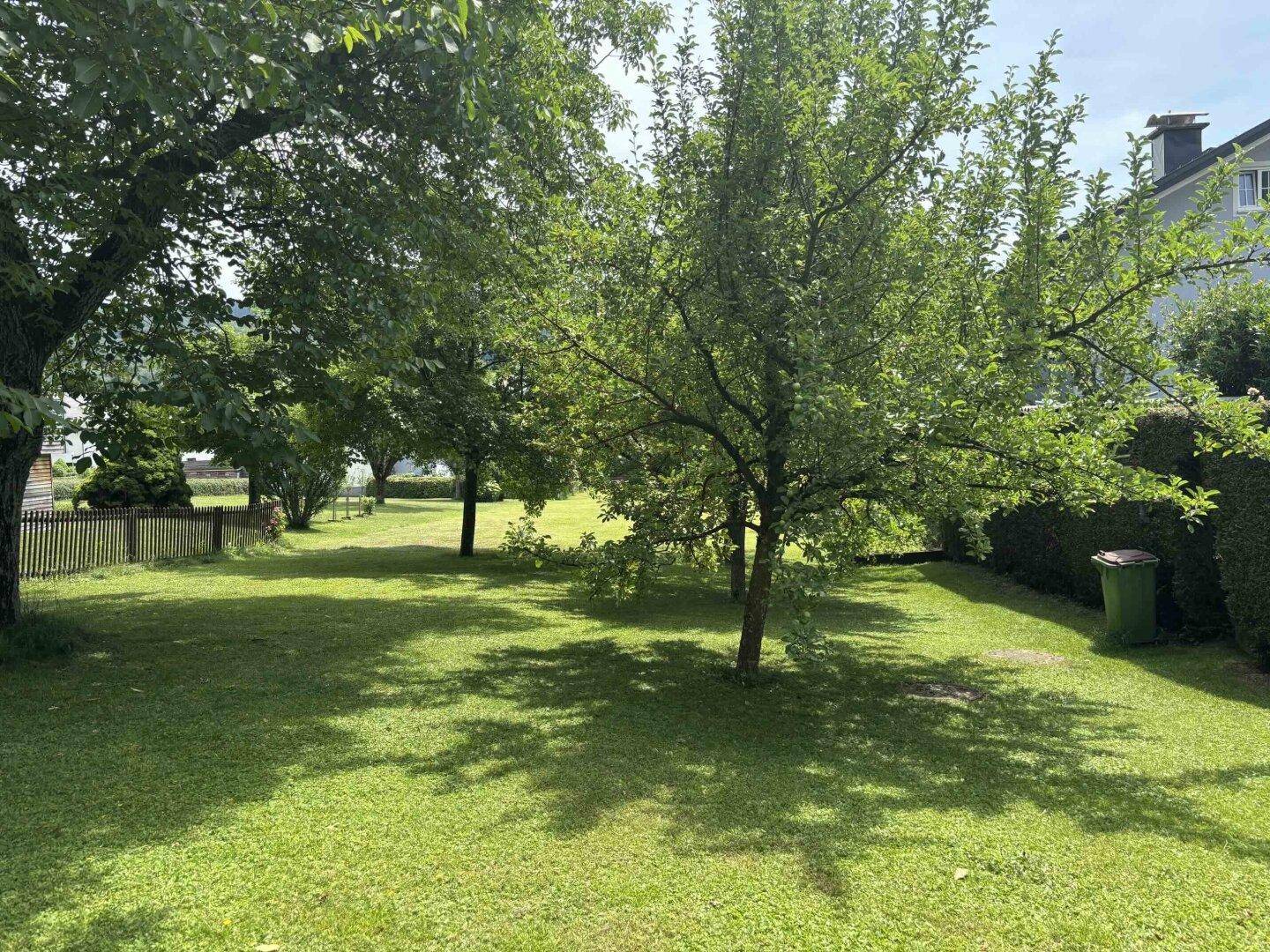 Weitläufiger Garten mit schattenspendenden Bäumen, gepflegtem Rasen und einem Haus im Hintergrund.