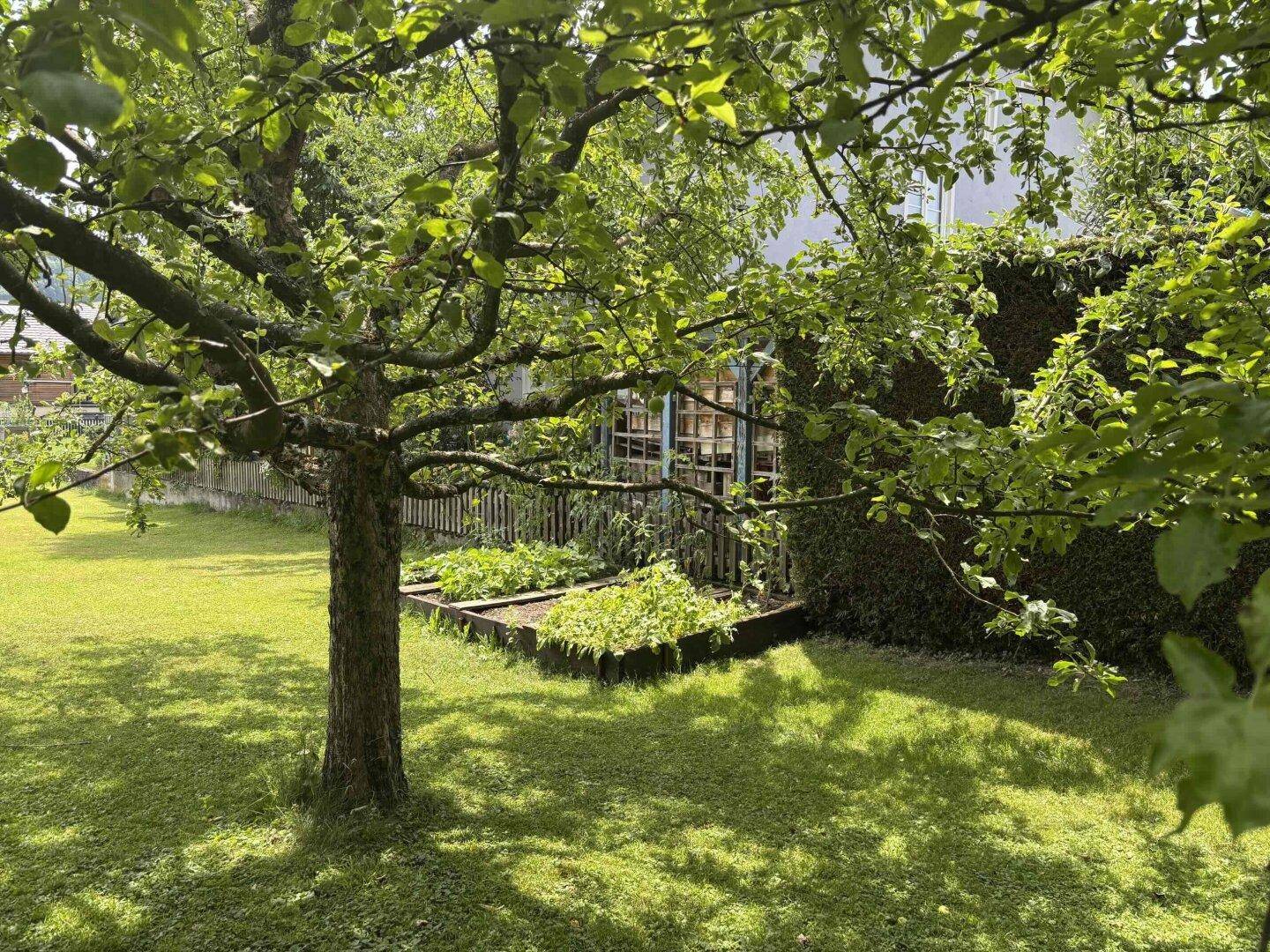 Idyllischer Gartenbereich mit Hochbeet für den Anbau von Gemüse und Obstbäumen im Vordergrund.