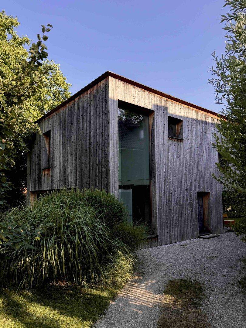 Modernes Holzhaus mit vertikaler Holzverkleidung, umgeben von üppigem Grün und einem Kiesweg.