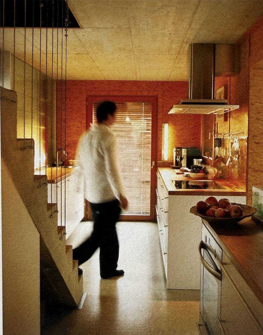 Schmale, moderne Küche mit Holzverkleidung, Edelstahlabzugshaube und Zugang zu einer Treppe.