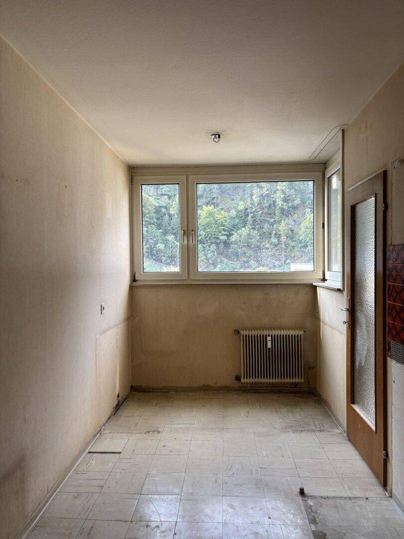 Leerer Raum mit Fliesenboden, Fenster und Heizkörper, bereit für eine neue Nutzung.