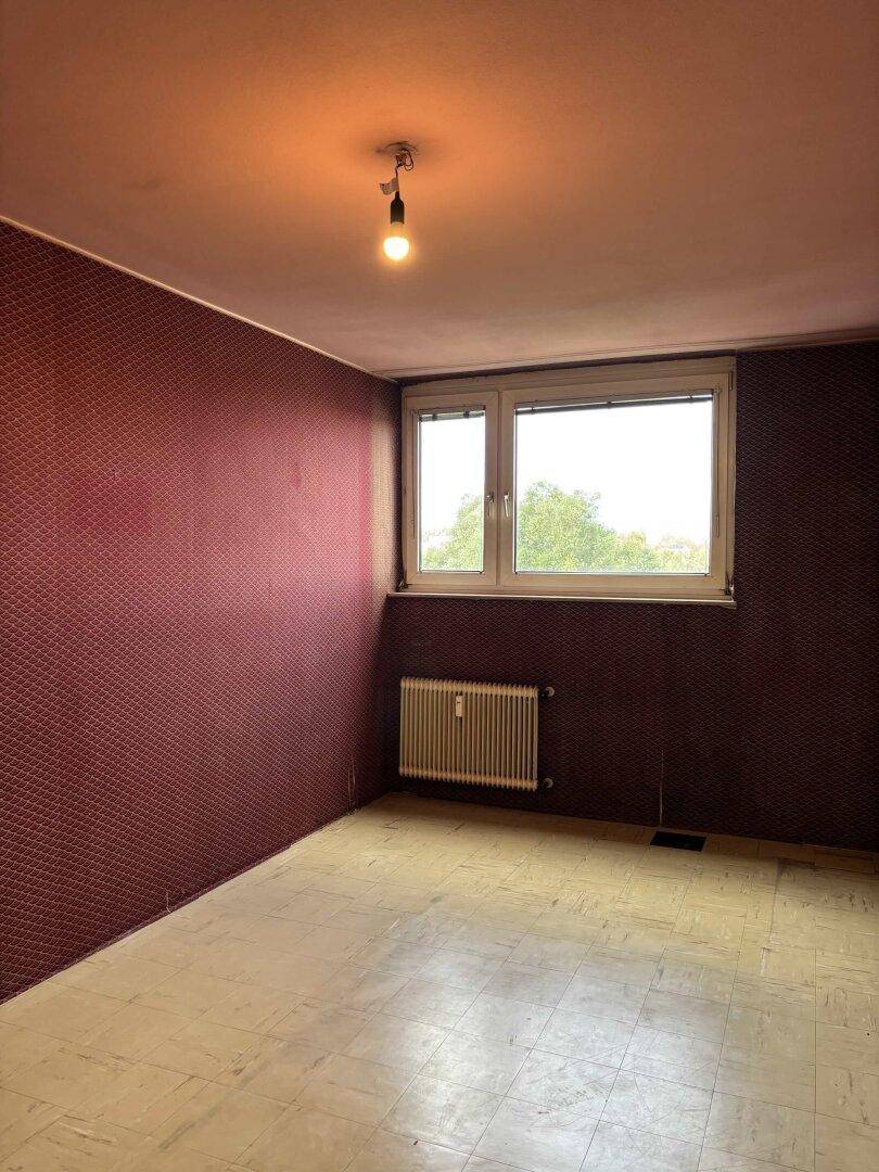 Schlafzimmer mit roter Tapete, Fenster und Heizkörper, bietet Potenzial zur Modernisierung.