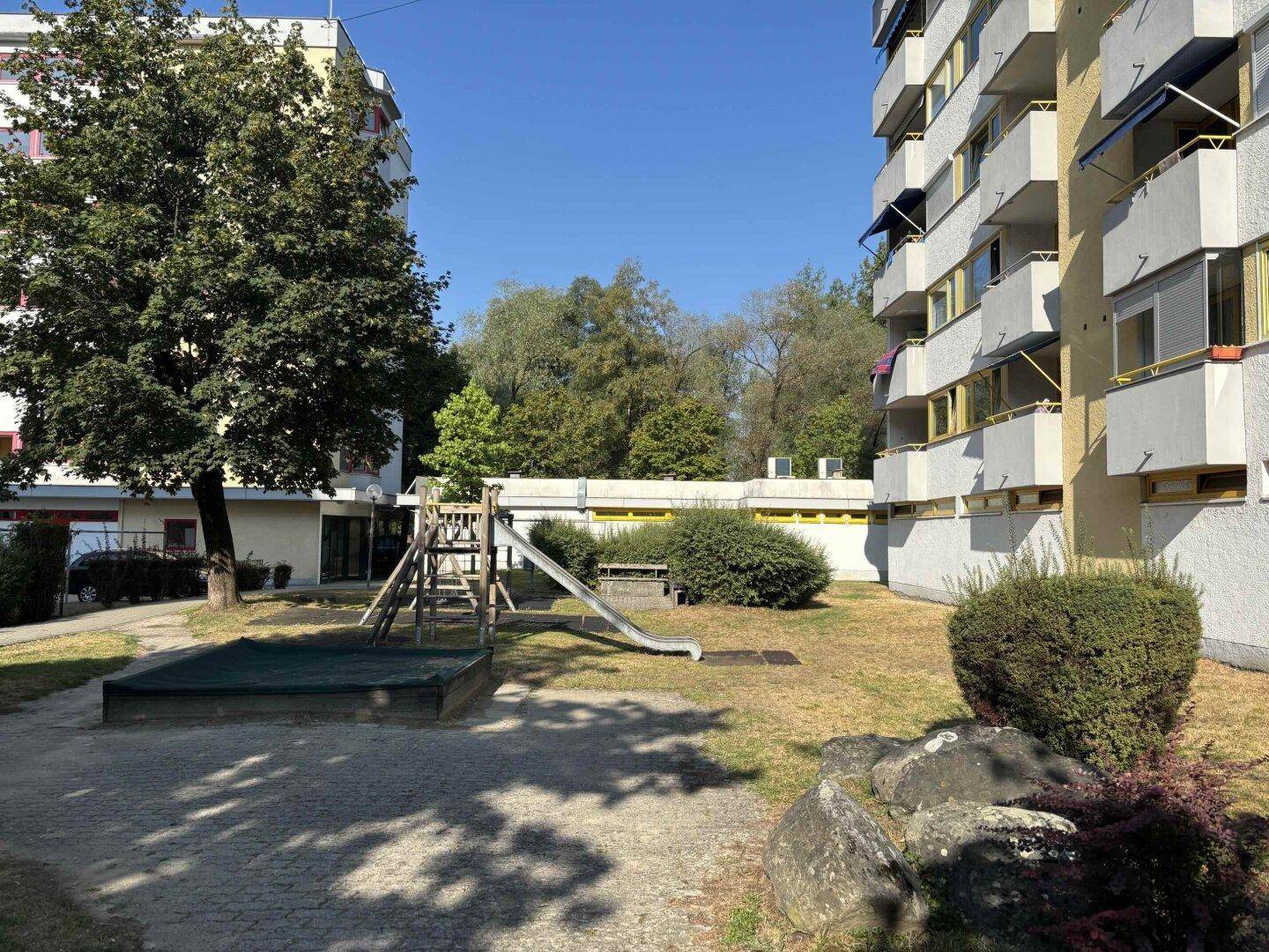 Kinderspielplatz mit Rutsche und Sandkasten, umgeben von Grünflächen.