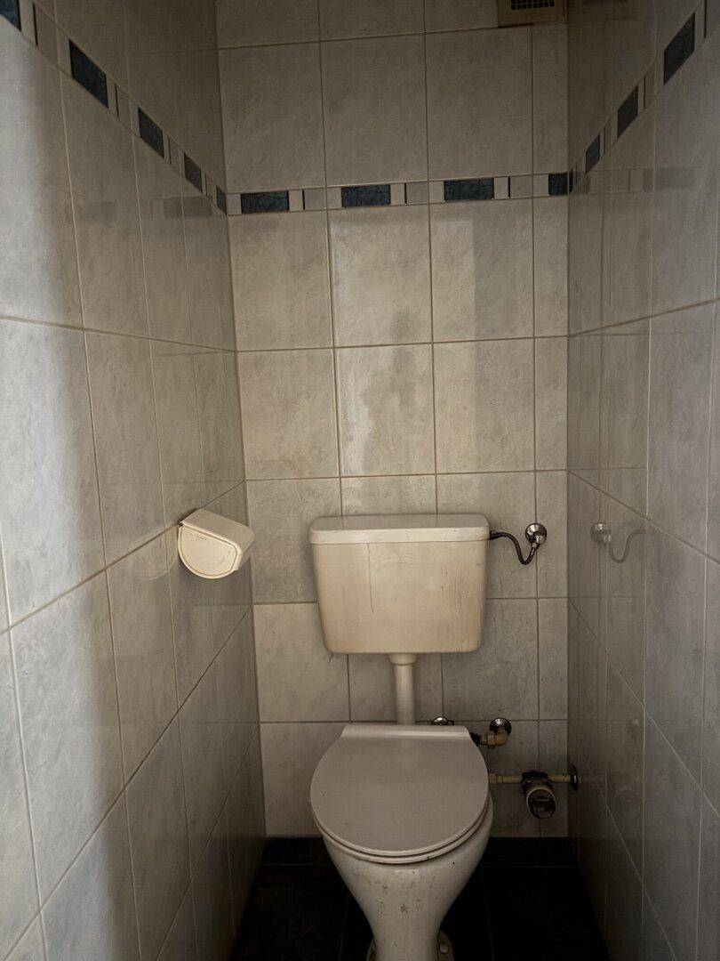 Separate Toilette mit Fliesen an Wänden und Boden, in schlichtem Design.
