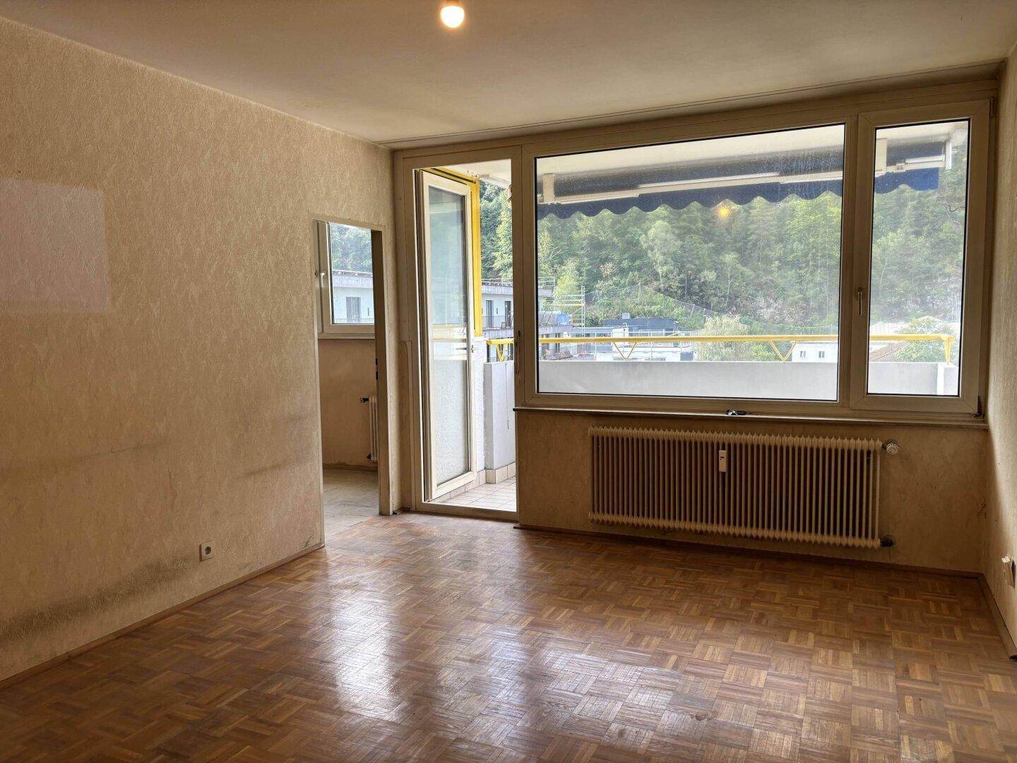 Helles Wohnzimmer mit Parkettboden, großem Fenster und Zugang zum Balkon.