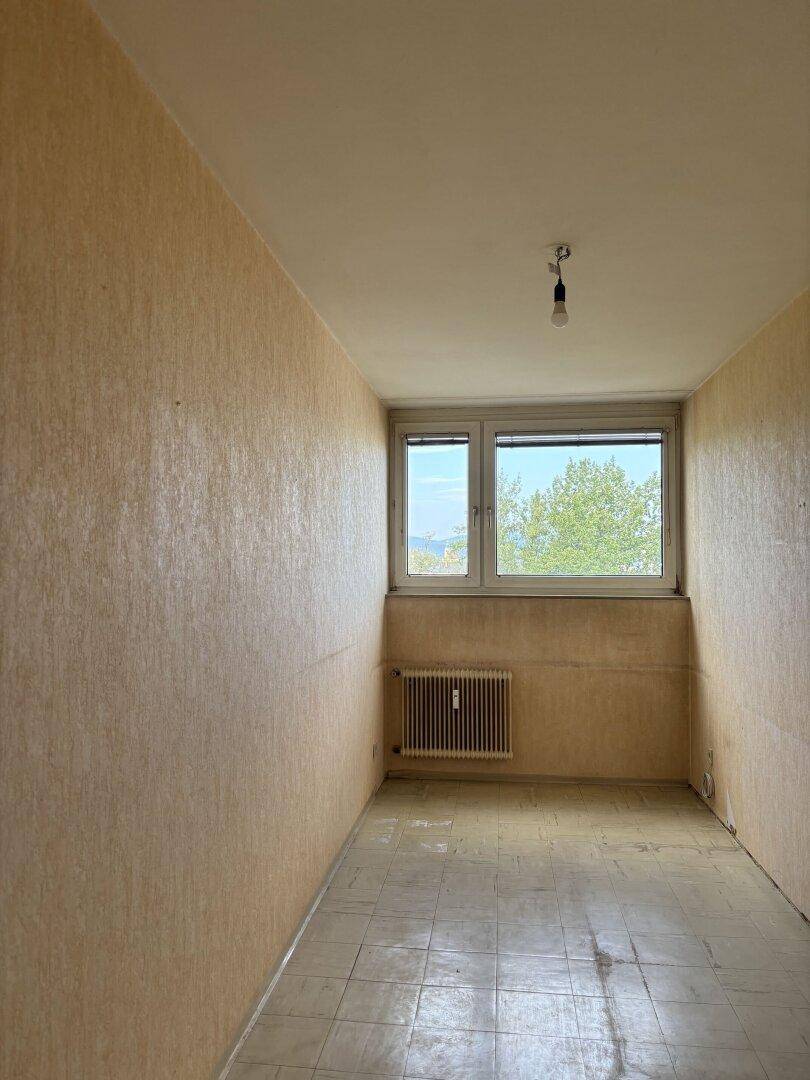 Leeres Zimmer mit Fenster, Heizkörper und Tapeten, ideal zur individuellen Gestaltung.