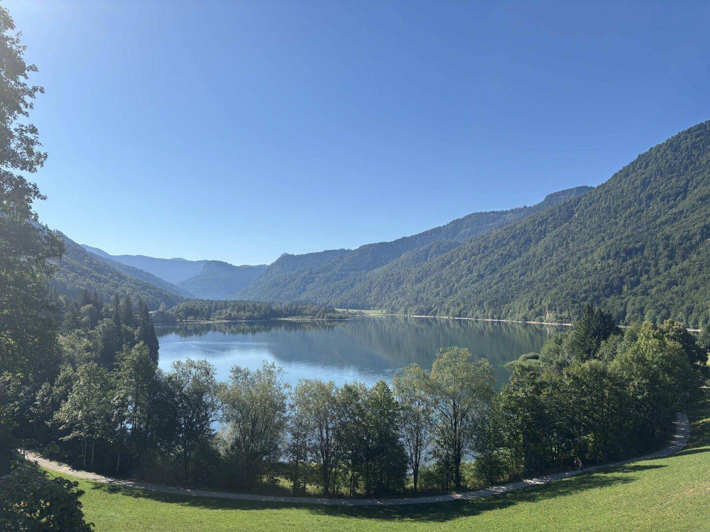 Malerischer See umgeben von bewaldeten Bergen unter strahlend blauem Himmel.