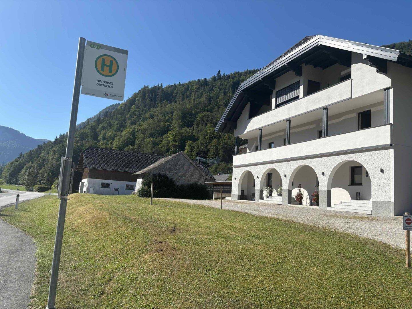Traditionelles Gebäude mit Arkaden und Balkonen neben einer Bushaltestelle in den Bergen.