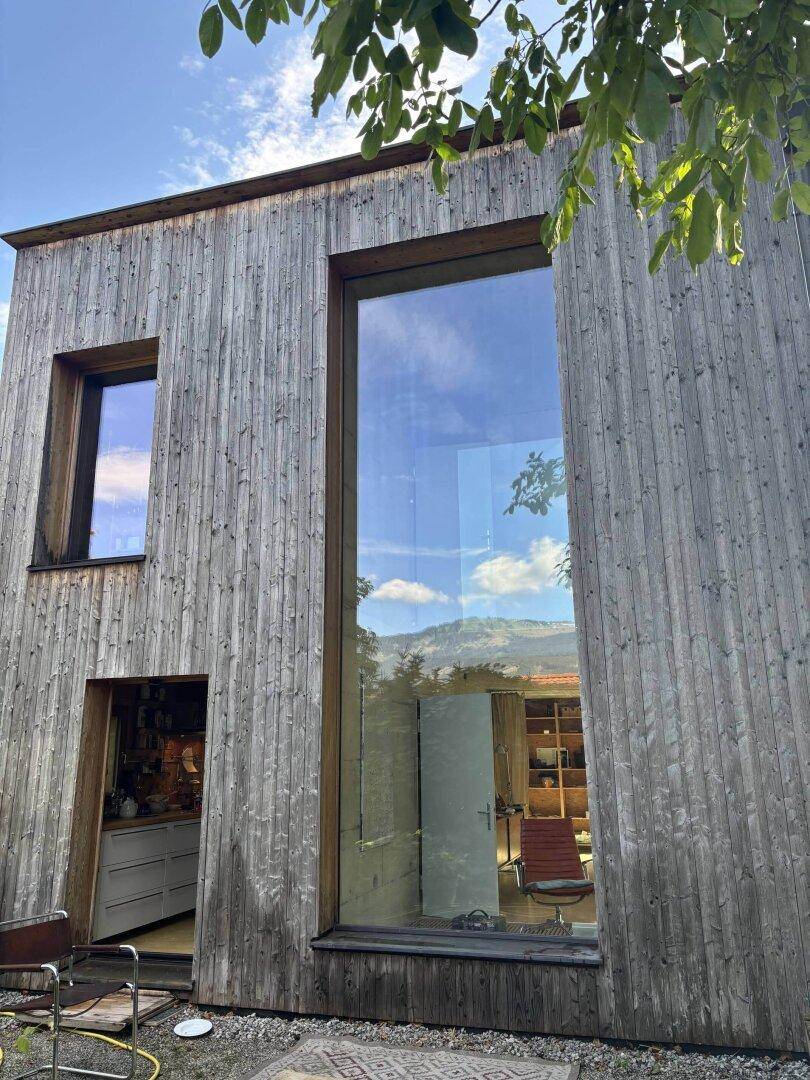 Fassade eines modernen Holzhauses mit großer Glasfront und Bergblick-Spiegelung.