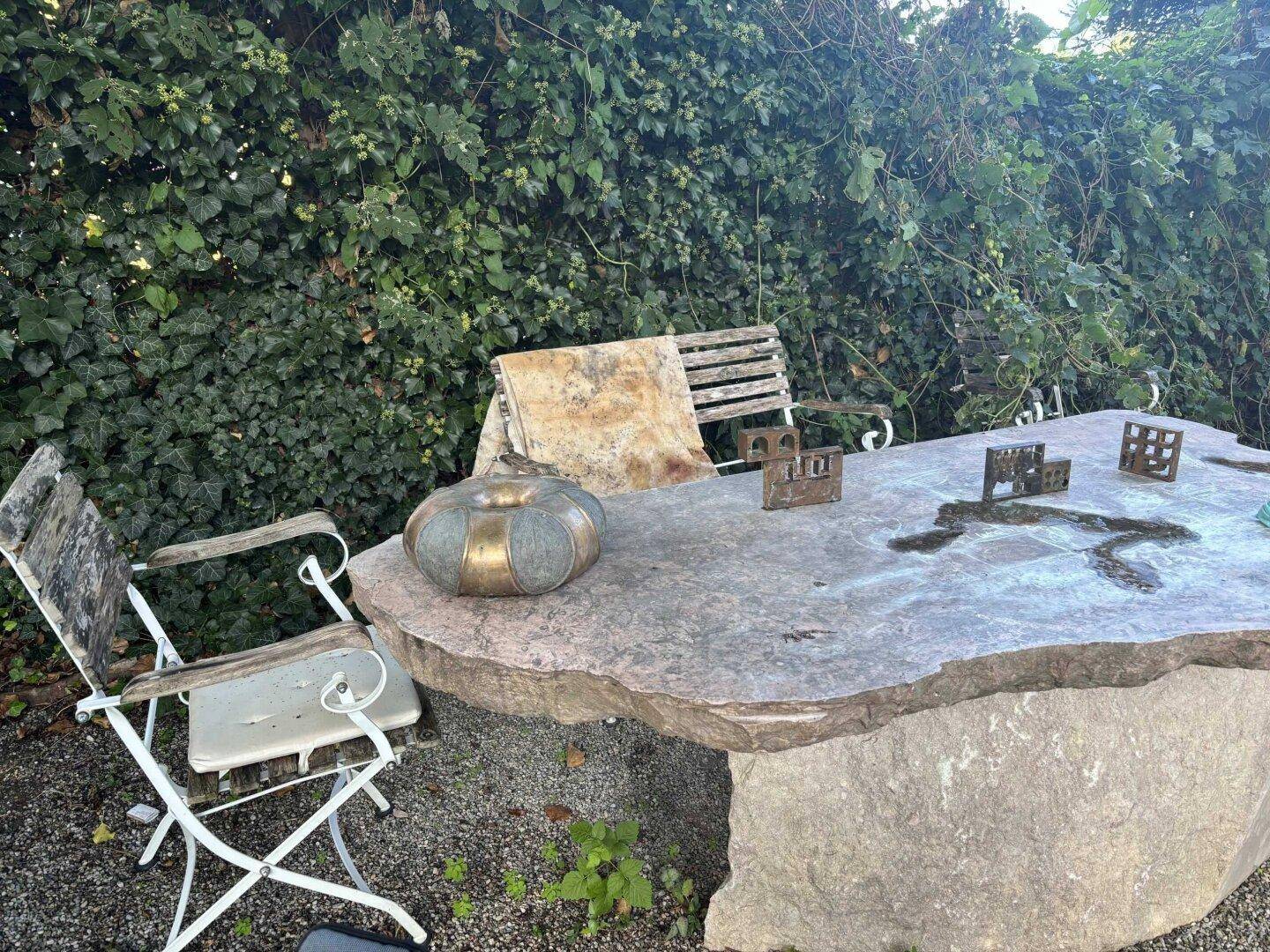 Rustikaler Steintisch mit Stühlen und Dekoration im Gartenbereich mit dichter Hecke.