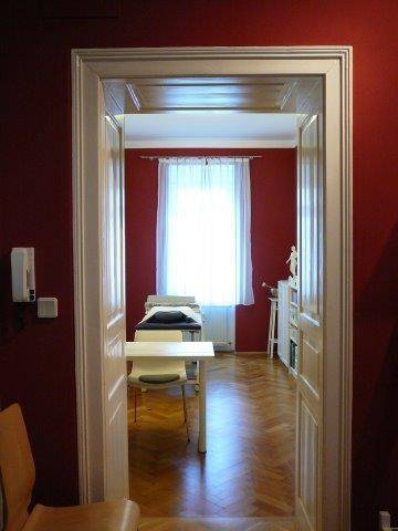 Durch eine Tür sichtbarer Raum mit roter Wand, Holzboden und einem Fenster.