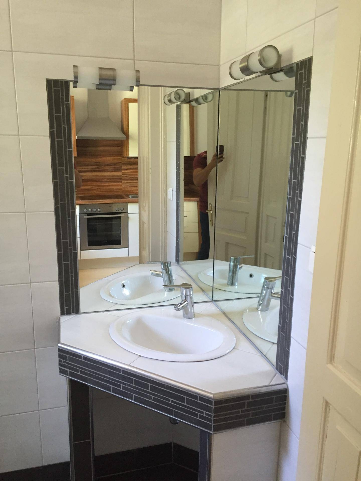 Badezimmer mit Eckwaschbecken, Spiegelschrank und Fliesen in Weiß und Grau.