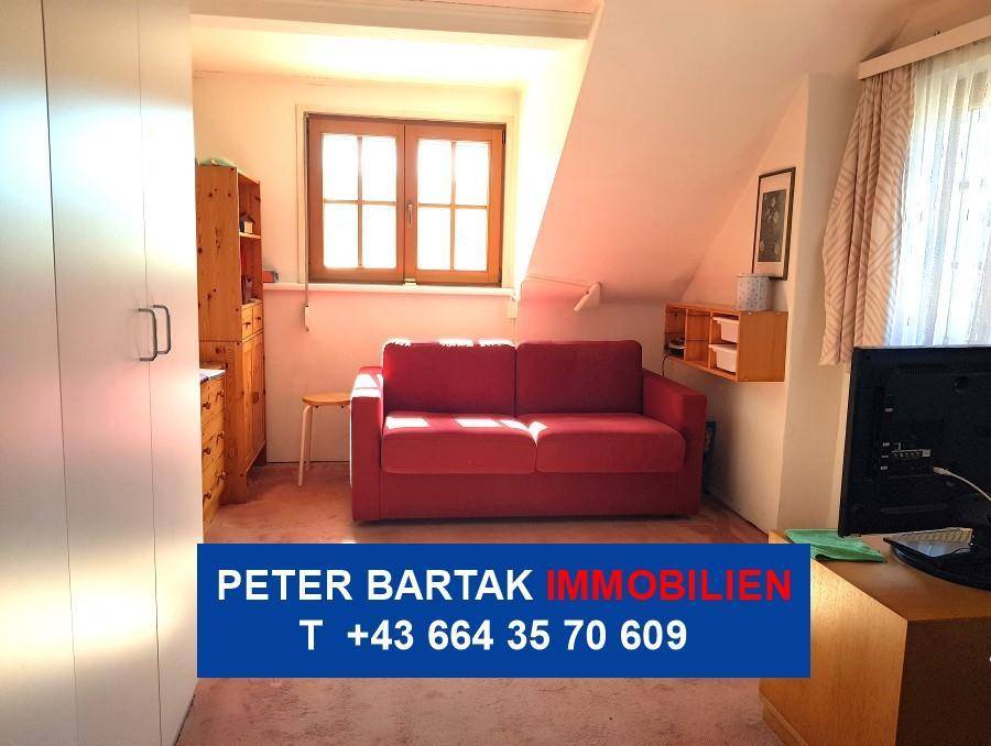Dachzimmer mit rotem Sofa, Schreibtisch und Stauraum unter der Schräge.