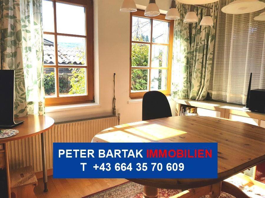 Heller Essbereich mit Holztisch, Stühlen und Blick in den Garten durch große Fenster.