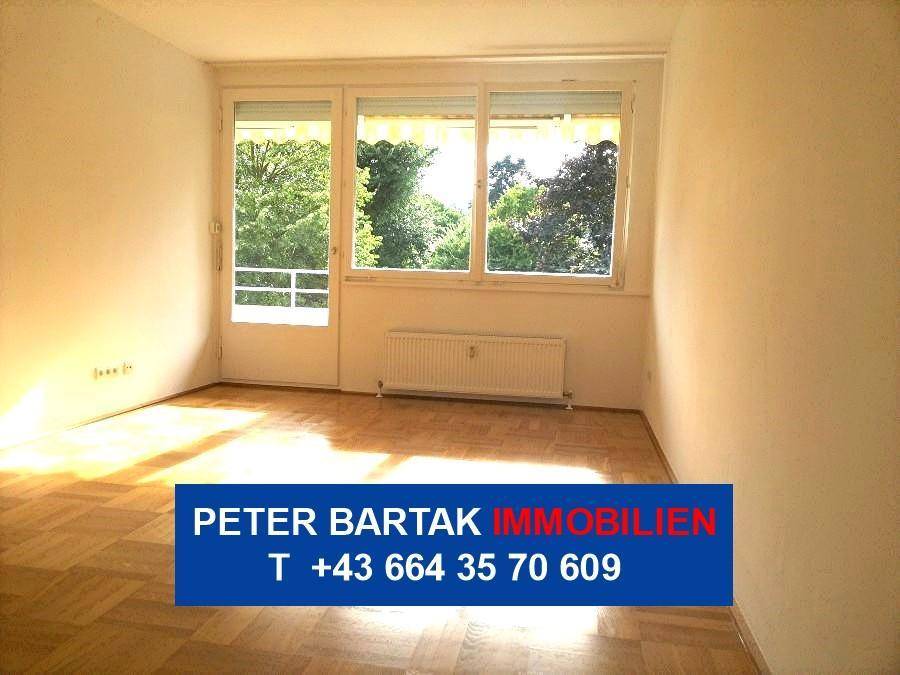 Helles Wohnzimmer mit Parkettboden und Zugang zu einem Außenbereich, umgeben von viel Grün.