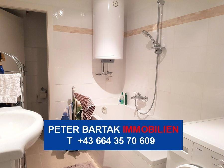 Badezimmer mit Badewanne, Duschfunktion und einem Warmwasserboiler an der Wand.