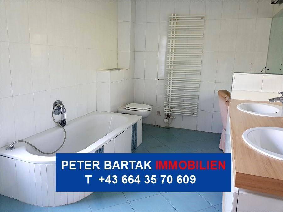 Geräumiges Badezimmer mit blauen Bodenfliesen, Badewanne, WC und Doppelwaschbecken.
