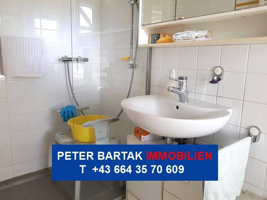 Helles Badezimmer mit weißen Fliesen, Waschbecken und Duschbereich.