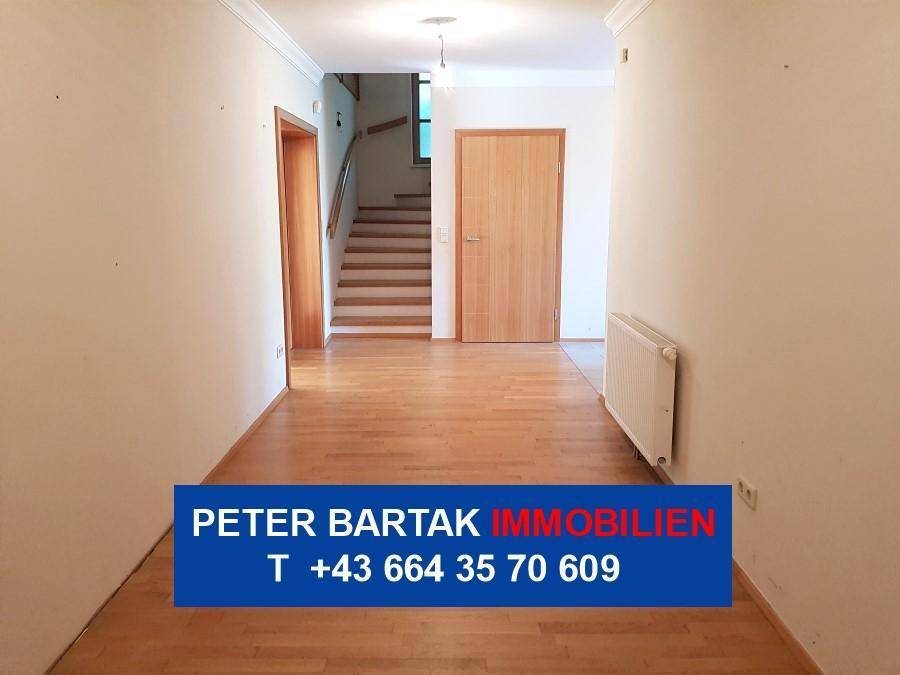 Geräumiger Flur mit Parkettboden, Holztreppe zum Obergeschoss und einer geschlossenen Tür.