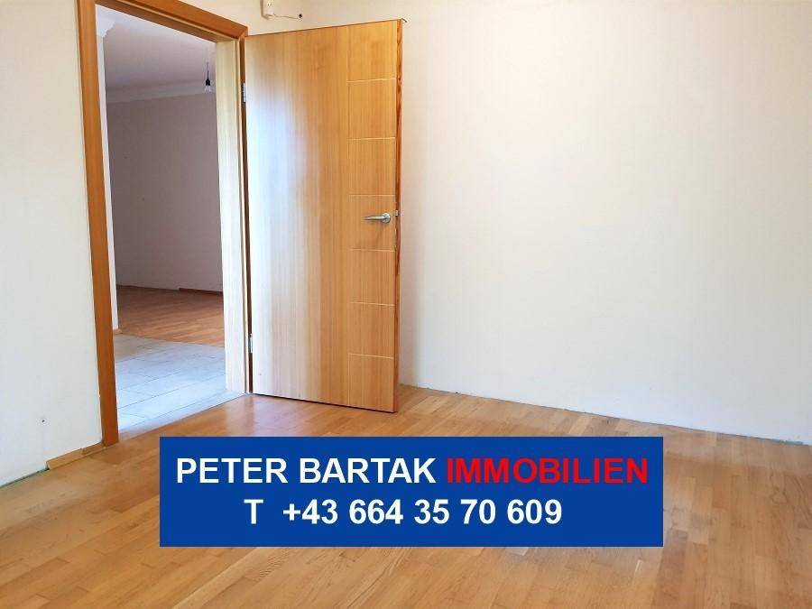Freundliches Zimmer mit Parkettboden und offener Holztür, bietet vielseitige Nutzungsmöglichkeiten.