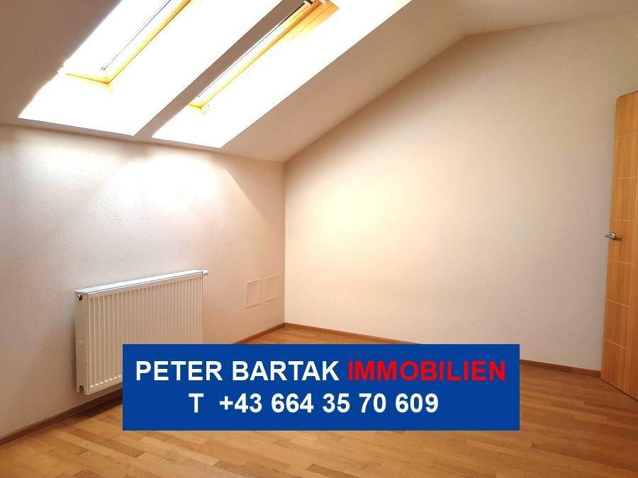 Geräumiges Dachzimmer mit Parkettboden, schräger Decke, Dachfenstern und Heizkörper.